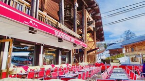 Een kabelbaan café met terras, houten architectuur en een besneeuwde berg op de achtergrond.