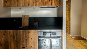 Een keuken met houten kastjes, een zwart aanrecht, een snijplank, een waterkoker en een vaatwasser.