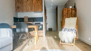 Een moderne keuken met houten kasten, een eethoek met tafel en stoelen, en een gezellige zithoek met een zachte fauteuil.