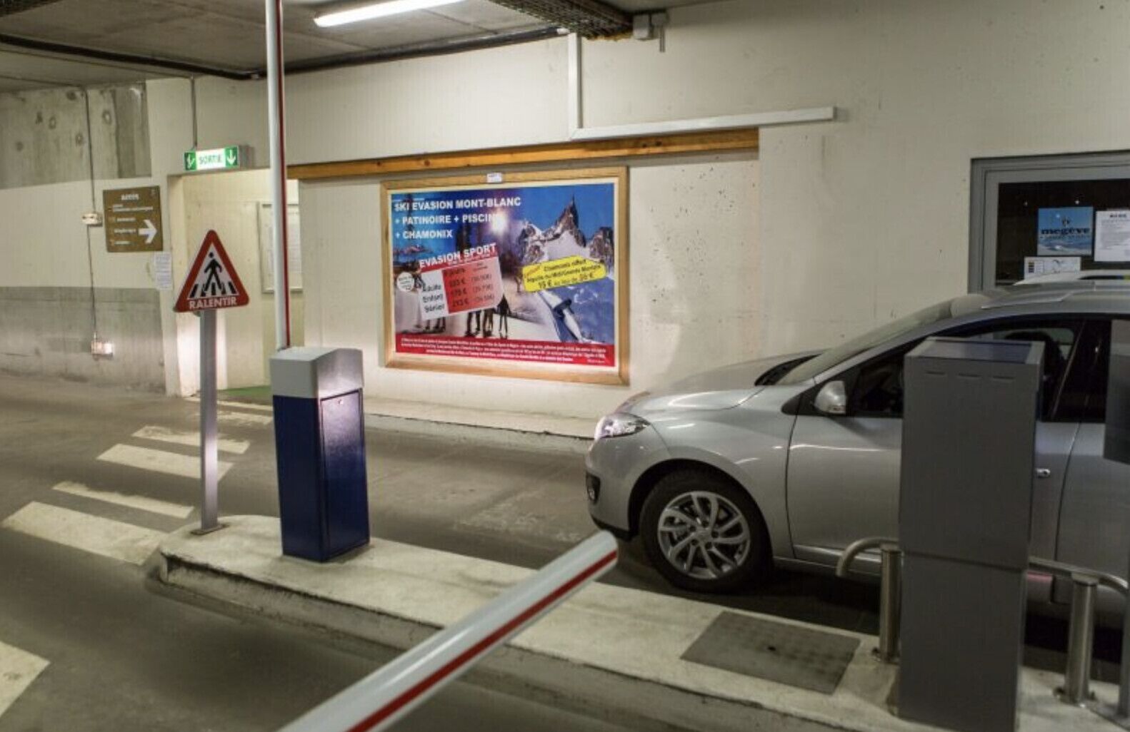 Un parcheggio con un'auto, un segnale di attraversamento pedonale e un poster che pubblicizza attività sugli sci.
