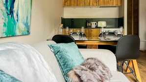 Een moderne woonkamer met een bank, een zacht kussen, en een eethoek met een houten tafel, stoelen en een koffieapparaat.