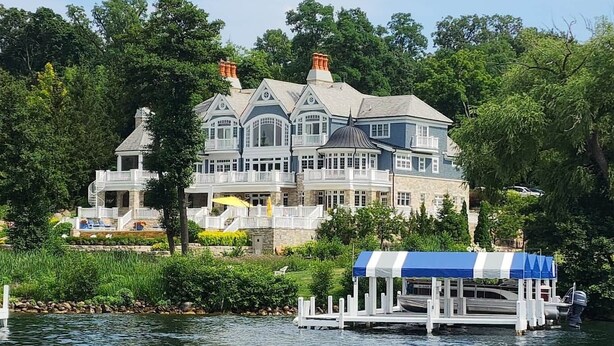 A large, multi-story house with a dock extending into a lake, surrounded by lush greenery. - Bayside Hideaway, Williams Bay, WI (Williams Bay)