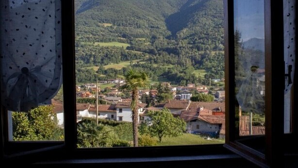 Vista a través de una ventana mostrando un paisaje montañoso con un pueblo abajo.