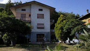 Un edificio de dos plantas con techo plano, un balcón en el piso superior y una puerta de garaje. Hay árboles y césped al frente del edificio.