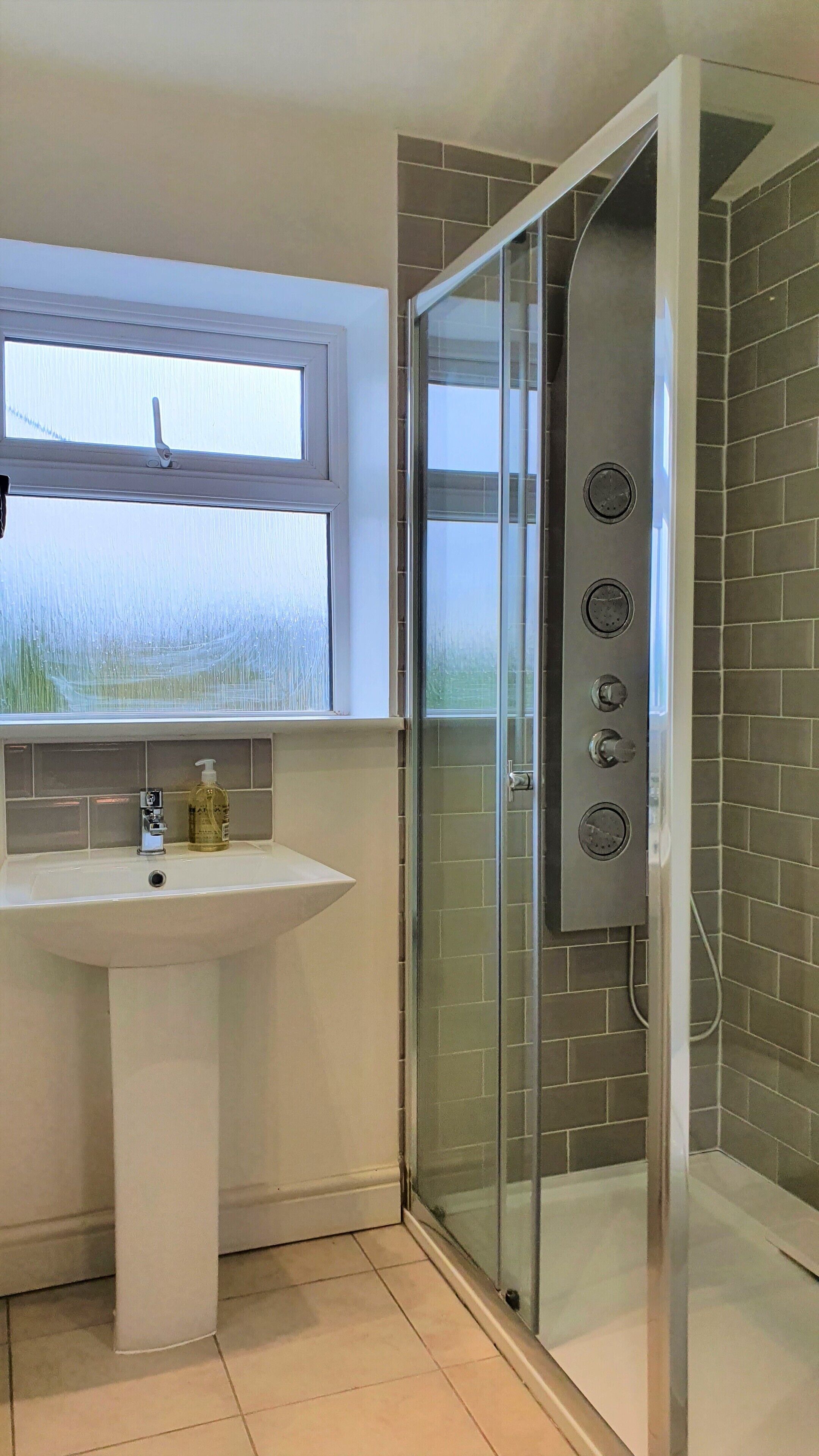 A modern bathroom with a glass-enclosed shower, a white sink, and a window above the sink.