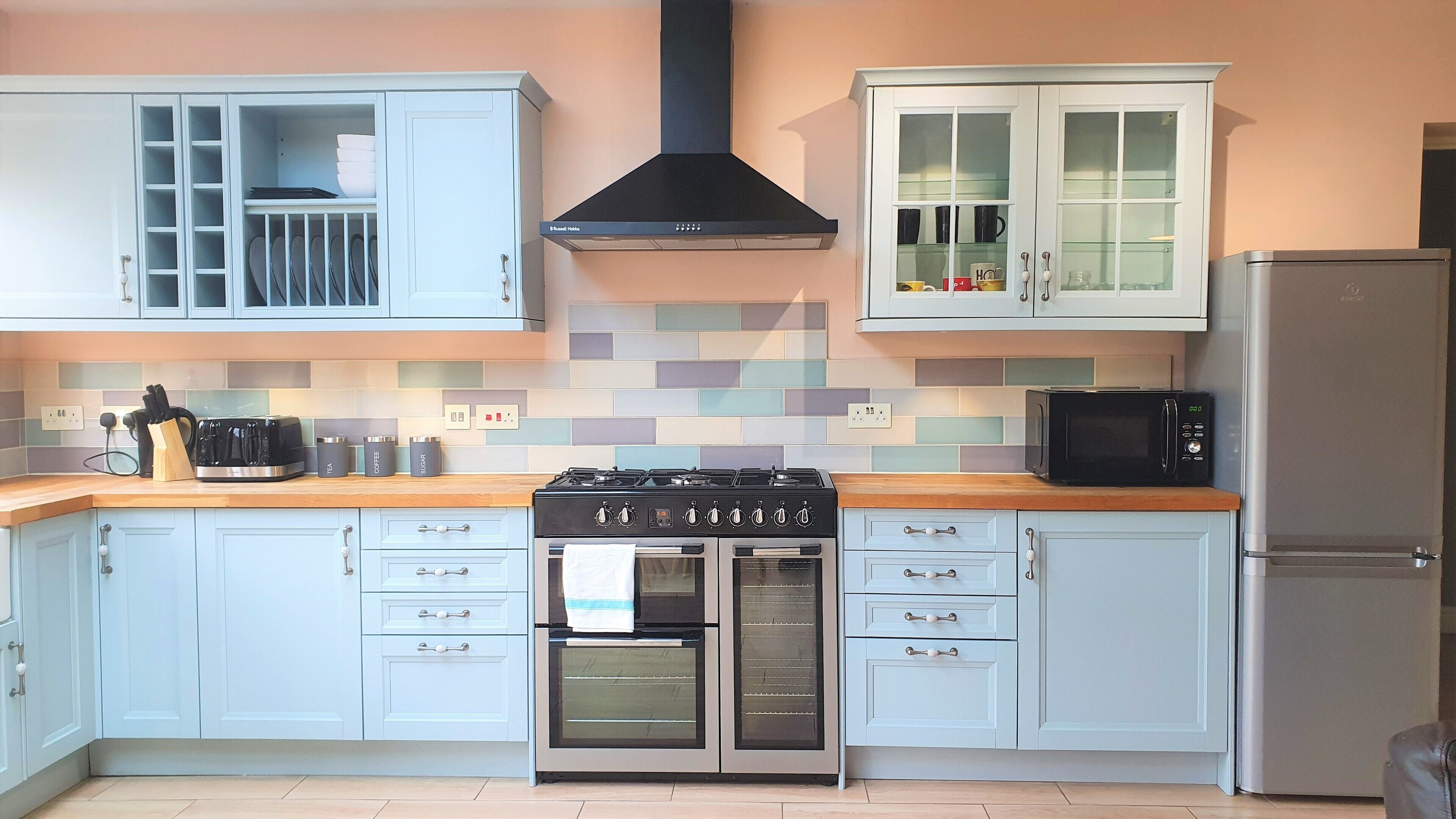 A kitchen with light blue cabinets, a black stove, a microwave, and a stainless steel refrigerator.