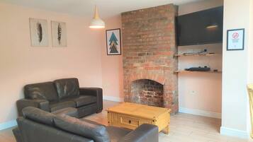 Ein Wohnzimmer mit Kamin aus Backstein, einer schwarzen Ledersofa, einem Couchtisch aus Holz und einem Wand-Fernseher.