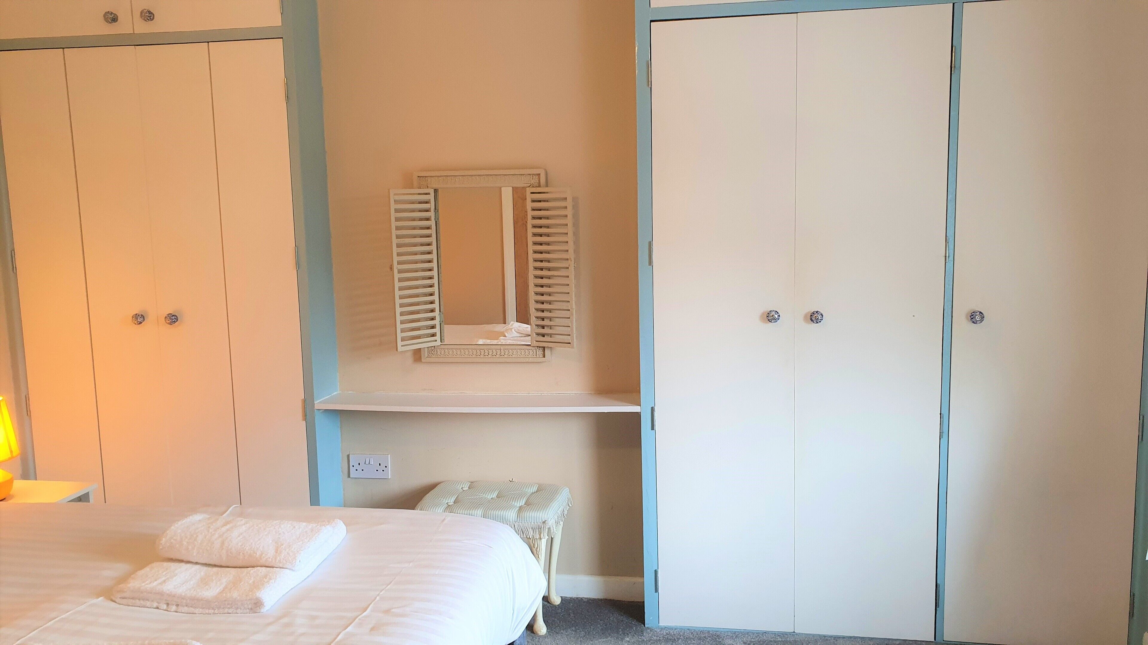 A bedroom with a bed, a bedside table, a mirror, and two wardrobes.