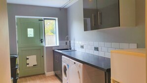 A compact kitchen with a washing machine, a sink, and a green door. - Large 5 Bedroom House Terrace Parking (Swindon)