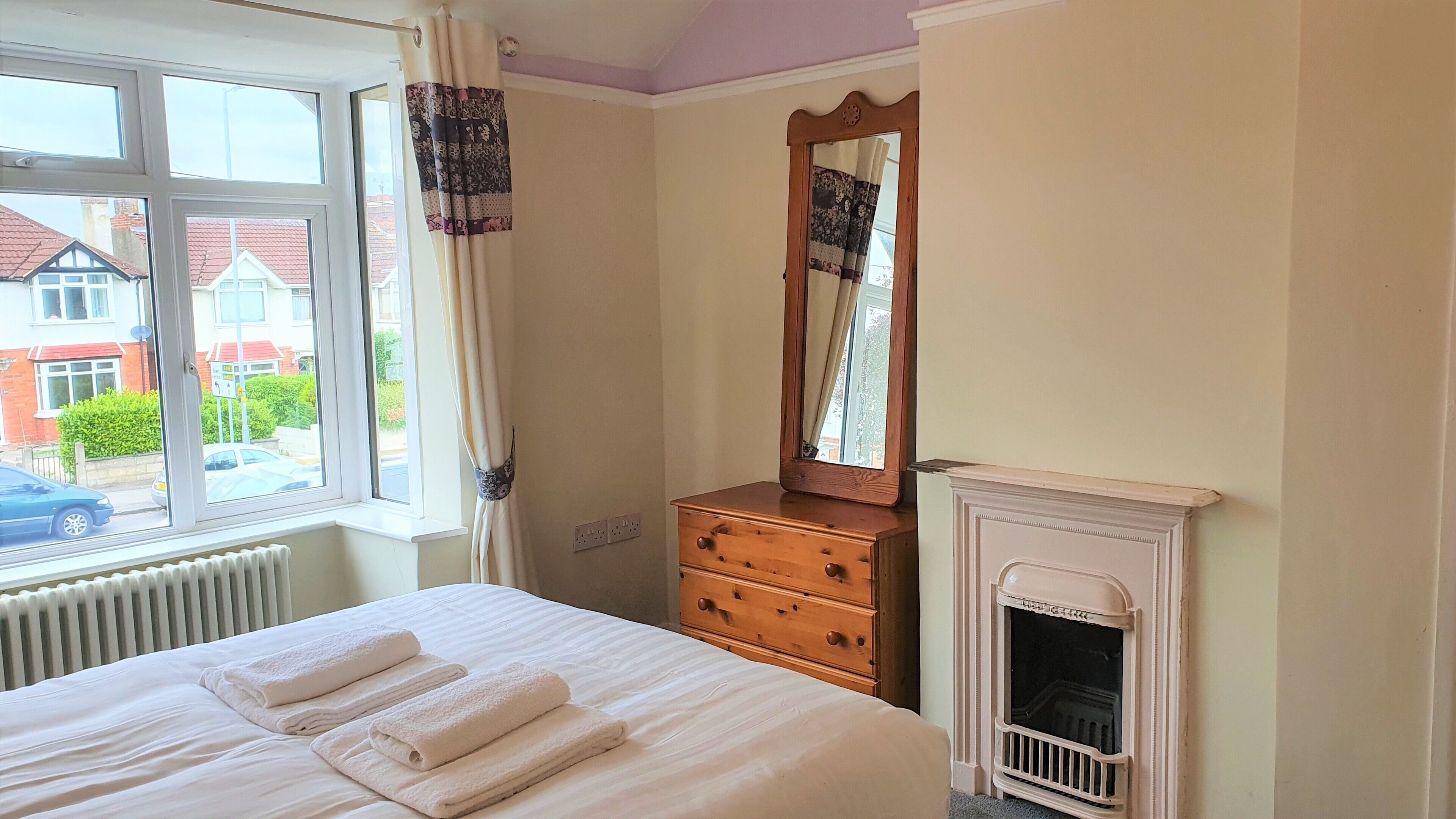 A bedroom with a bed, a dresser, a mirror, and a fireplace.
