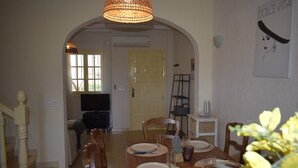 Een eetruimte met een houten tafel gedekt voor vier personen, een kroonluchter en een schilderij aan de muur.