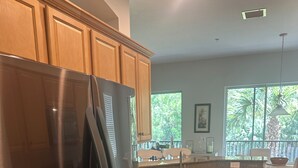 A kitchen with wooden cabinets, a stainless steel refrigerator, a granite countertop, and a window with a view of trees. - Gorgeous 2nd Floor Unit in The Quarry, Minutes to downtown Naples and Mercato. (Naples)