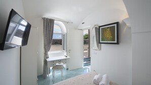 Un dormitorio con cama, televisor, baño con lavamanos y vista al exterior.