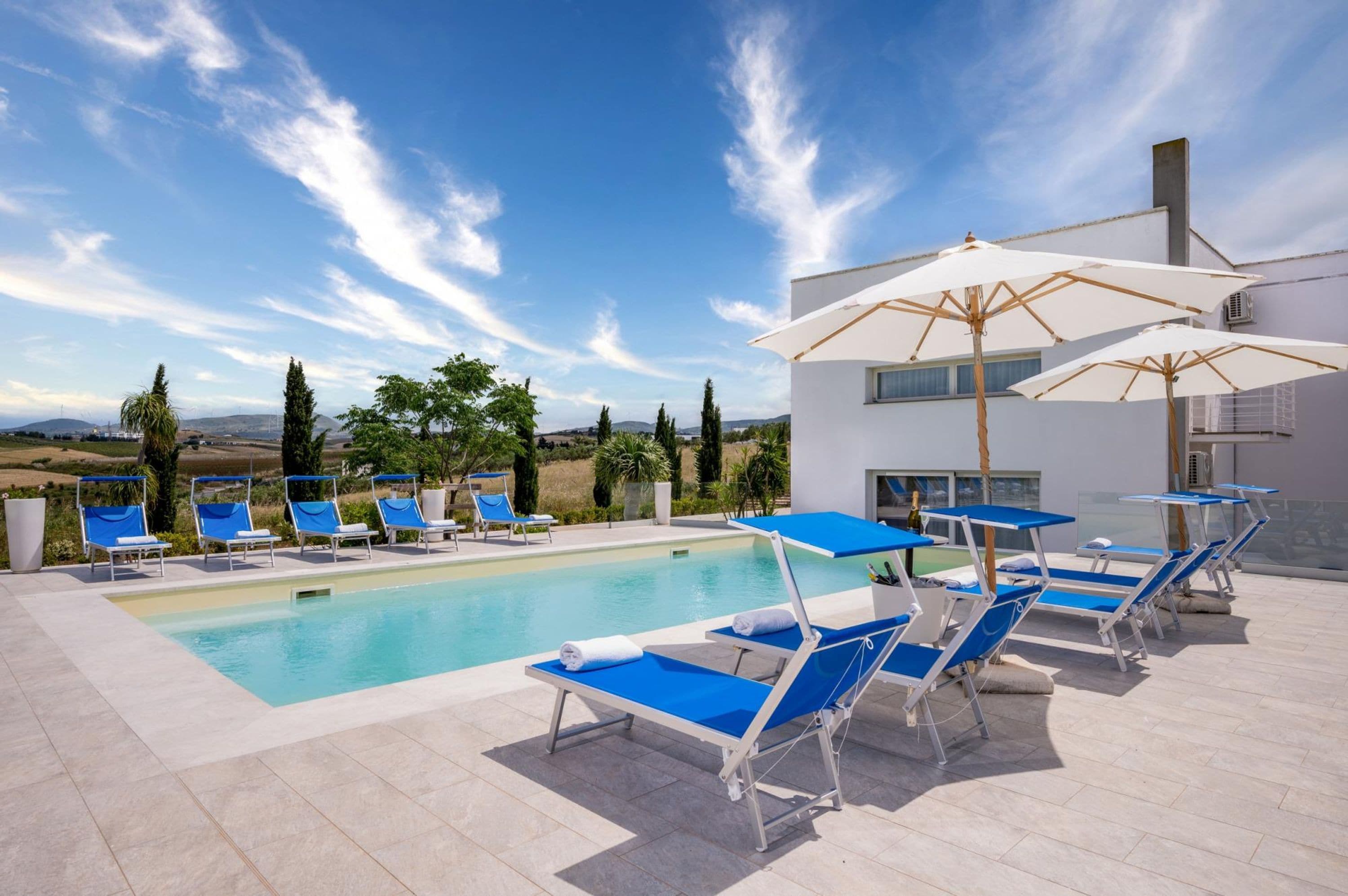 A poolside area with lounge chairs and umbrellas, a clear sky, and a view of the countryside.