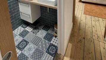 A compact bedroom with a sloped ceiling, a small bathroom with a sink and mirror, and a patterned floor.
