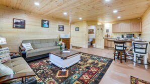 L’intérieur chaleureux d’un chalet comprend un salon avec un canapé, une table basse et un coin cuisine doté de meubles en bois et d’un bar.