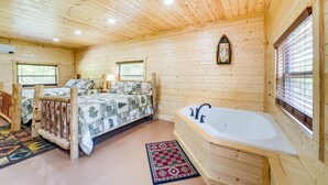 Une chambre dans une cabane en bois, avec un lit, une fenêtre à cadre en bois, une baignoire en bois et un plafond en bois.