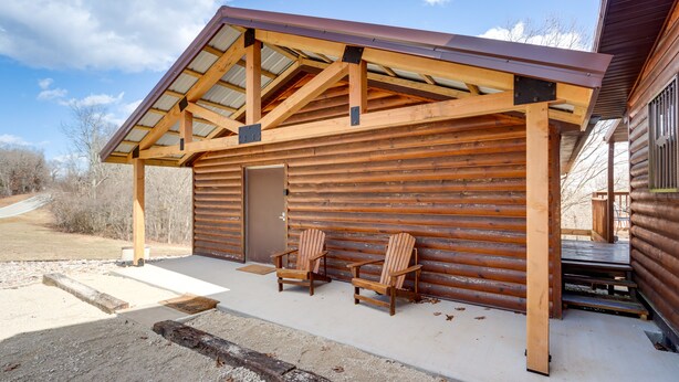 Une cabane en bois avec un porche couvert et deux chaises.