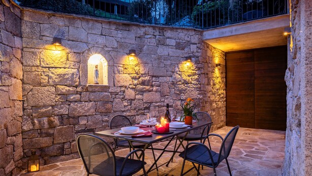 A stone-walled outdoor dining area with a table set for four, chairs, and wall-mounted lighting. - Ca' Luigia boutique apartment in Montorfano (Mergozzo)