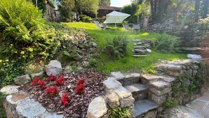 A garden with stone walls, red flowers, and a grassy area with outdoor furniture. - Ca' Luigia boutique apartment in Montorfano (Mergozzo)