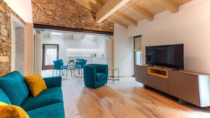 Una sala de estar moderna con una pared de piedra, vigas de madera, un sofá, un televisor y un comedor.