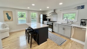 A modern kitchen with a central island, built-in appliances, and large windows offering views of greenery. - Lakefront Home on Lake Iroquois (Hinesburg)