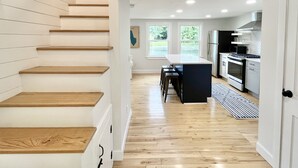 A modern kitchen with wooden flooring, a central island, and a staircase with wooden steps. - Lakefront Home on Lake Iroquois (Hinesburg)