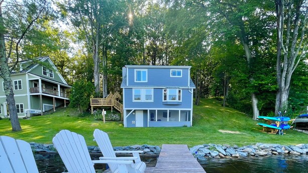 A wooden dock leading to a house with a deck, surrounded by trees and a body of water. - Lakefront Home on Lake Iroquois (Hinesburg)