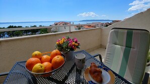 Un balcón con una mesa dispuesta para el desayuno, con naranjas, un croissant y una taza.