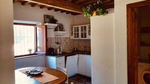 Een kleine keuken met een houten tafel, witte kastjes en een raam dat natuurlijk licht binnenlaat.