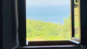Een uitzicht op een groen landschap en de zee vanuit een raam.