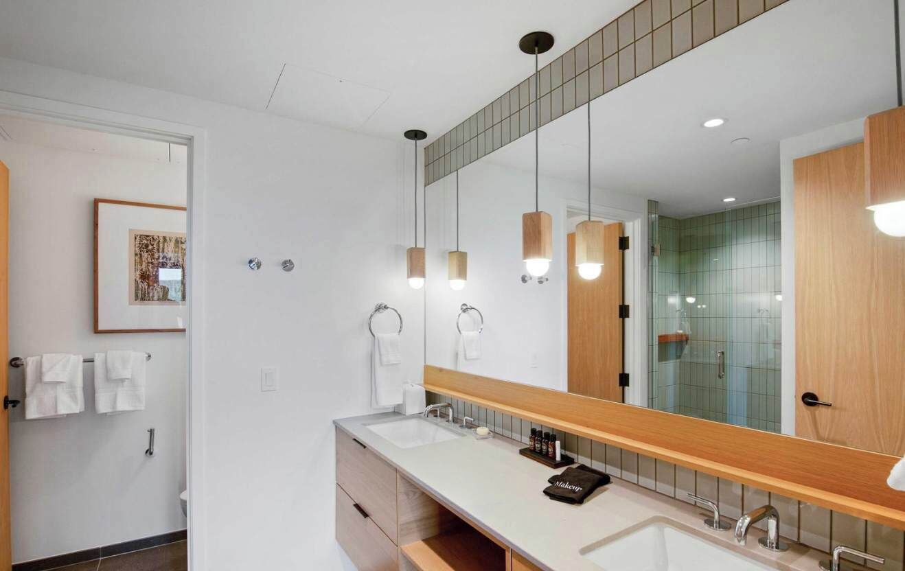 Une salle de bain moderne avec un grand miroir, deux vasques et des luminaires suspendus.