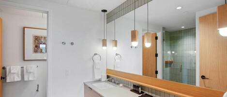 Une salle de bain moderne avec un grand miroir, deux vasques et des luminaires suspendus.