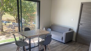 A modern living room with a glass table, two chairs, a grey sofa, and a wooden floor. - Maison Climatisée Avec Piscine Entre Montalivet et Soulac (Grayan-et-l'Hôpital)