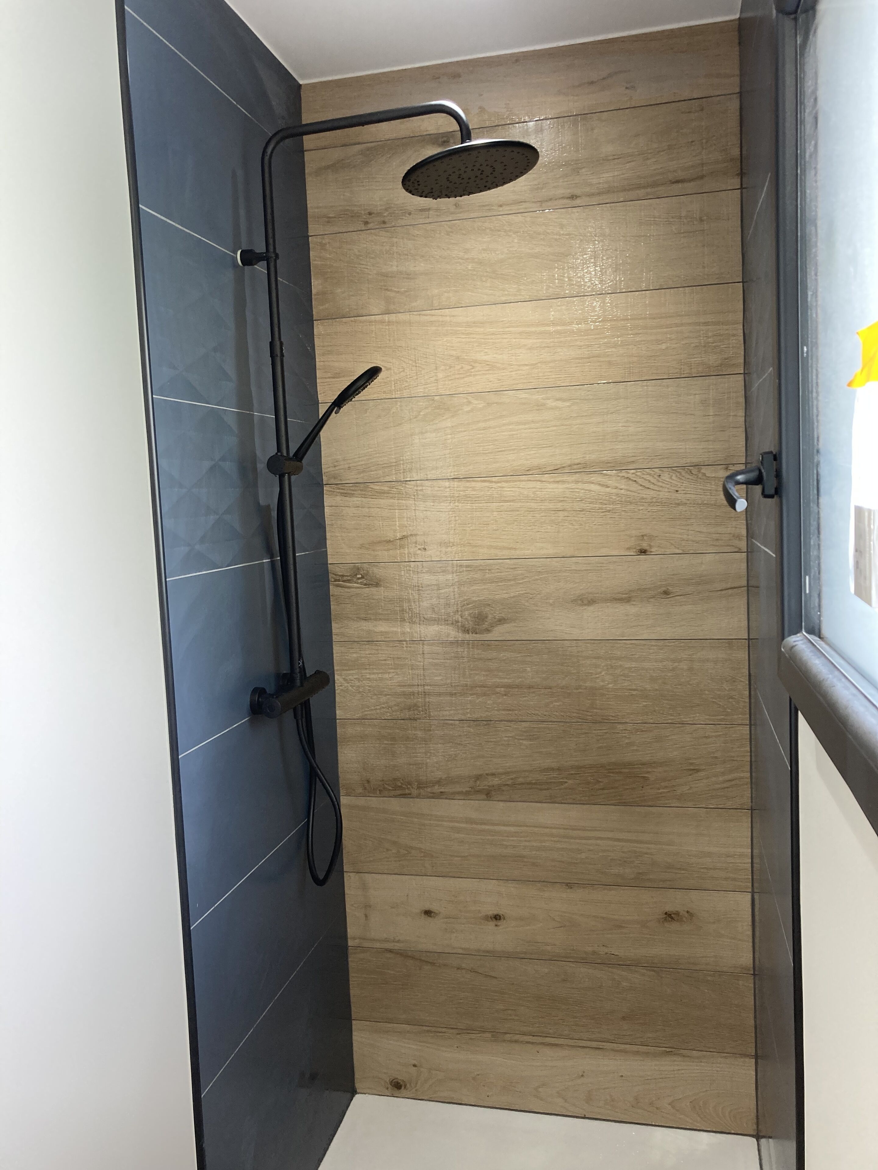 A shower with a wooden panel wall, a black tiled wall, and a door with a handle.