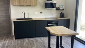 A modern kitchen with dark cabinets, a wooden countertop, a black sink, and a built-in oven. - Maison Climatisée Avec Piscine Entre Montalivet et Soulac (Grayan-et-l'Hôpital)