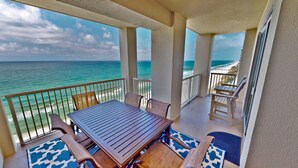 A balcony with a view of the ocean, a wooden table, and wicker chairs. - Million dollar views, sleeps 10! Beachfront corner unit @ Grand Panama Resort! (Panama City Beach)