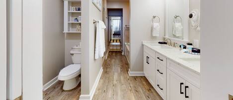 A modern bathroom with a wooden floor, white fixtures, and a visible toilet.