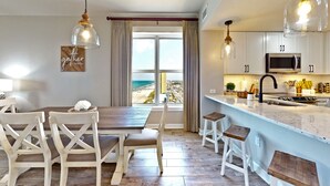 A modern kitchen with a large window, white cabinetry, and a dining area with wooden chairs and a table. - Million dollar views, sleeps 10! Beachfront corner unit @ Grand Panama Resort! (Panama City Beach)