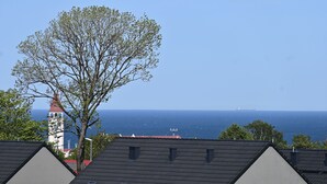 A residential area with houses having sloped roofs and skylights, a large tree, and a distant view of the sea. - Family Homes - Apartament Sea View (Wladyslawowo)