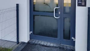 A modern building entrance with a dark blue door, a metal gate, and a clear glass window. - Family Homes - Apartament Sea View (Wladyslawowo)