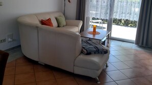 A living room with a sofa, a table with a candle, a painting on the wall, and a view through a glass door.