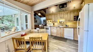 A modern kitchen with wooden cabinets, a dining table with chairs, and a large window. - Cozy cabin w/ Trailer, Sleeps 6 - 10 guests, Walking Distance to Beach, Hot Tub! (Swansea Point)