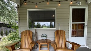 A porch with two wooden Adirondack chairs, a small round table, and a decorative tree. - Cozy cabin w/ Trailer, Sleeps 6 - 10 guests, Walking Distance to Beach, Hot Tub! (Swansea Point)
