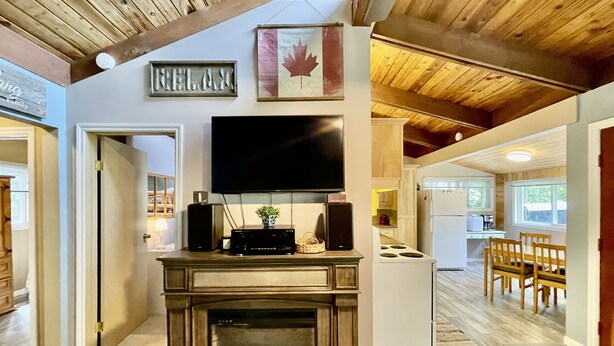 A cozy living room with a fireplace, a mounted TV, and a wooden ceiling. - Cozy cabin w/ Trailer, Sleeps 6 - 10 guests, Walking Distance to Beach, Hot Tub! (Swansea Point)