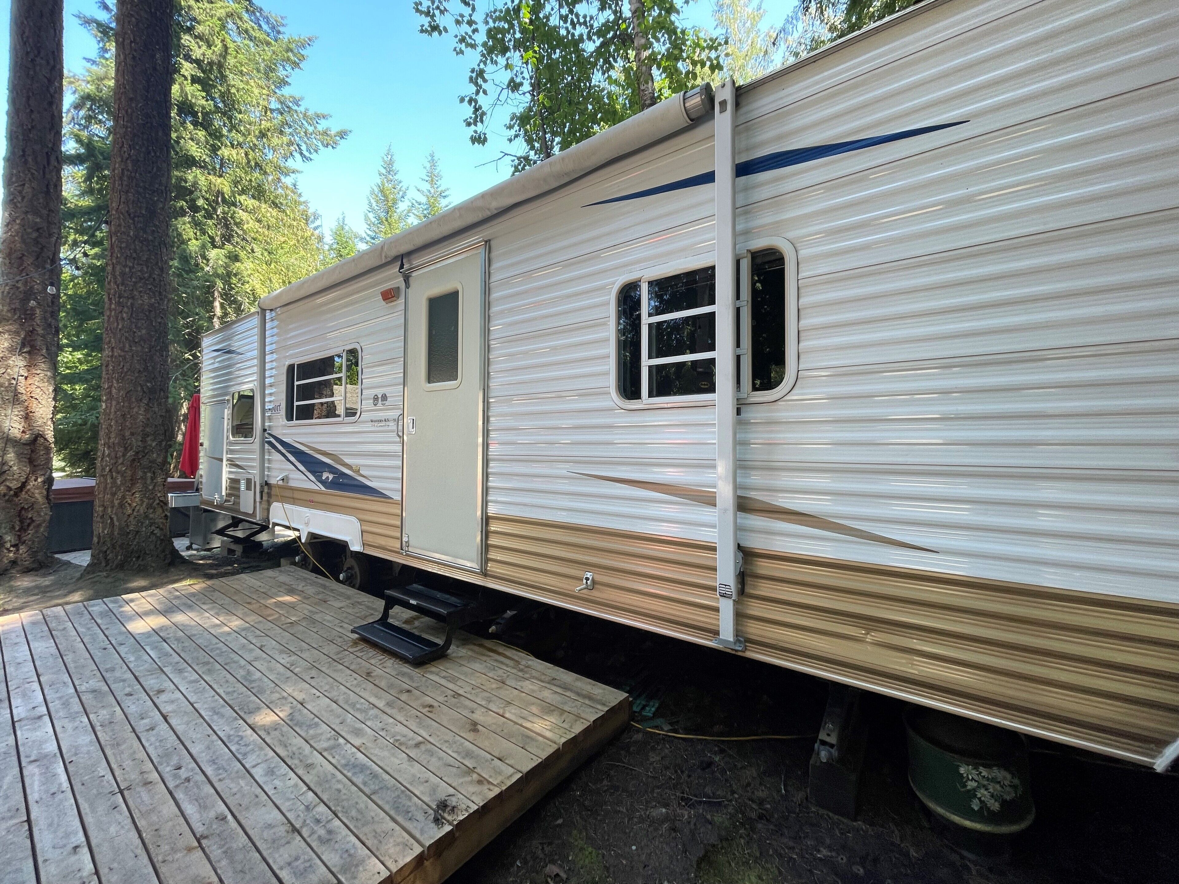 Een stilstaande camper met een houten terras, een klein raam en een deur.