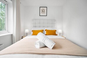 A hotel room with a large bed, two bedside lamps, a window, and a framed picture on the wall.