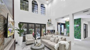 A spacious living area with a large sofa, armchairs, and a coffee table. There are large windows and a view of the outdoors. - Tiki Las Olas, Fort Lauderdale (Fort Lauderdale)