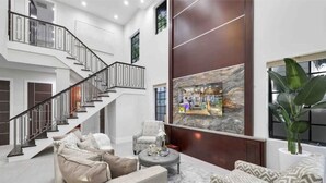 A spacious living area with a staircase, a seating area with a patterned sofa, and a large artwork on the wall. - Tiki Las Olas, Fort Lauderdale (Fort Lauderdale)