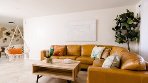 A living room with a brown leather sofa, a wooden coffee table, a hanging chair, and a large green plant. - ༄The Agave Ranch༄ FREE Pool Heating & Arcade Room! (Phoenix)
